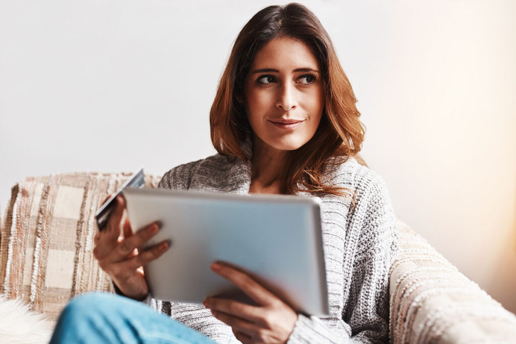 Shot of an attractive young woman using a digital tablet and credit card on the sofa at home